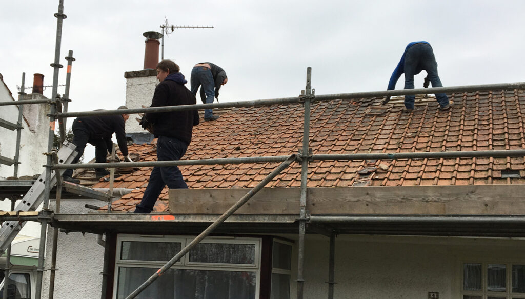 Workmen removing old tiles from bungalow